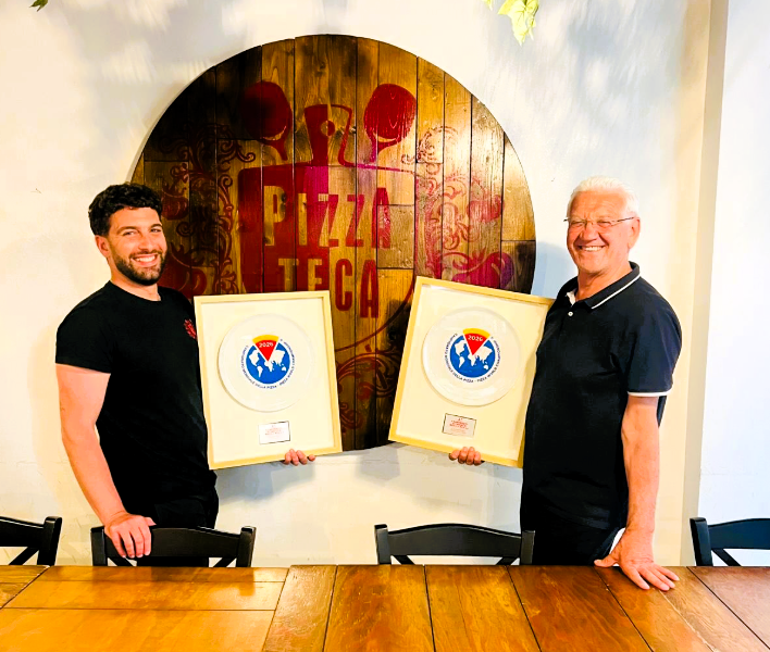 NUOVO RICONOSCIMENTO INTERNAZIONALE PER ANDREA GALLIZZI DI ROCCA DI BOTTE: MEDAGLIA D'ARGENTO AL CAMPIONATO MONDIALE DELLA PIZZA 78 Due uomini con premi in un pizzeria.
